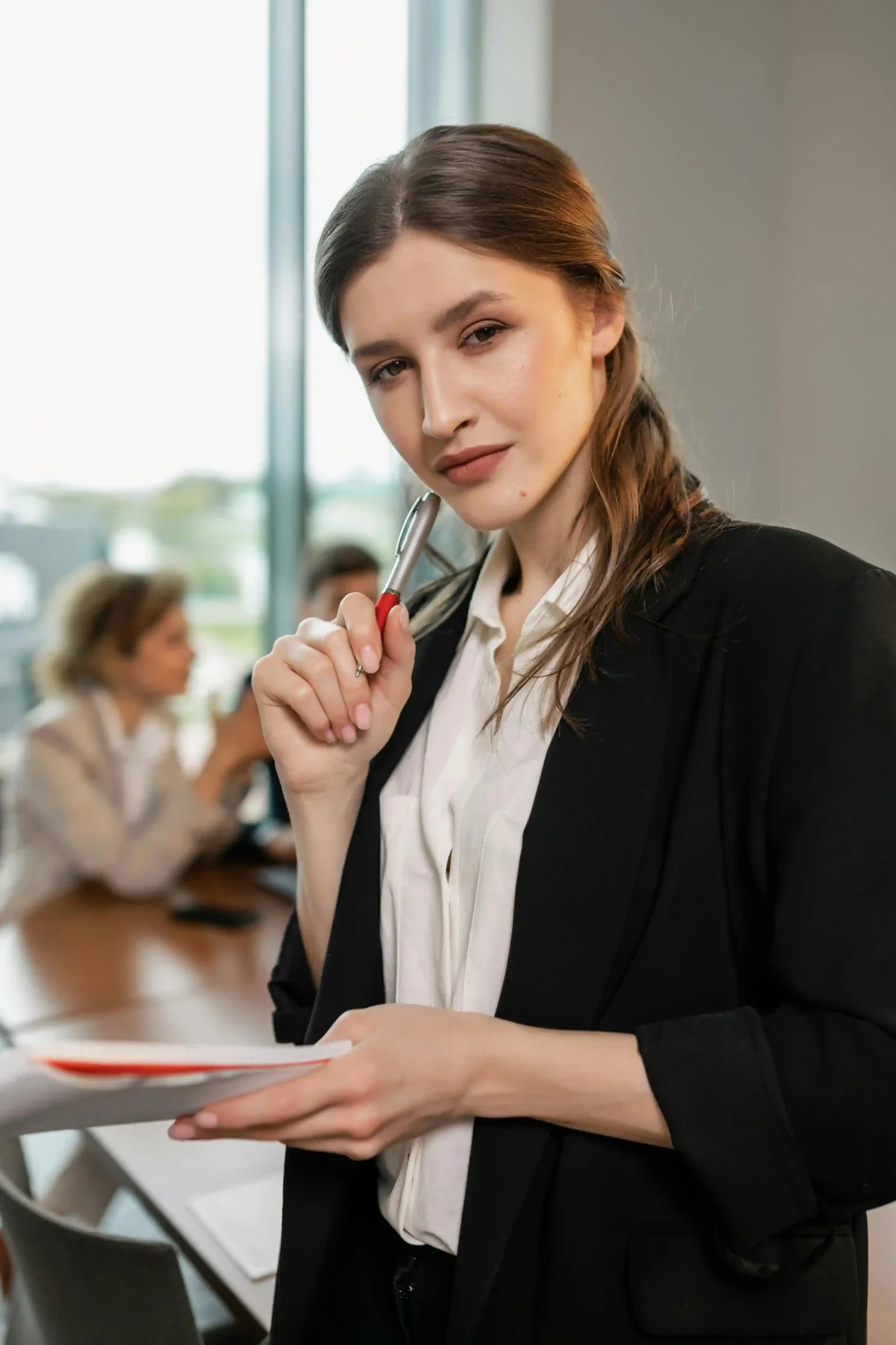 A confident businesswoman holding documents and a pen in a meeting room.