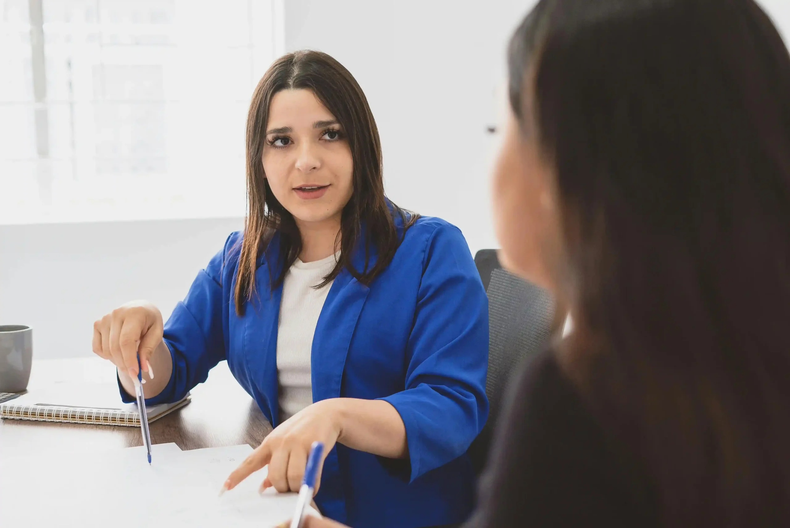 A woman in a blue blazer discussing documents with a colleague at a table.