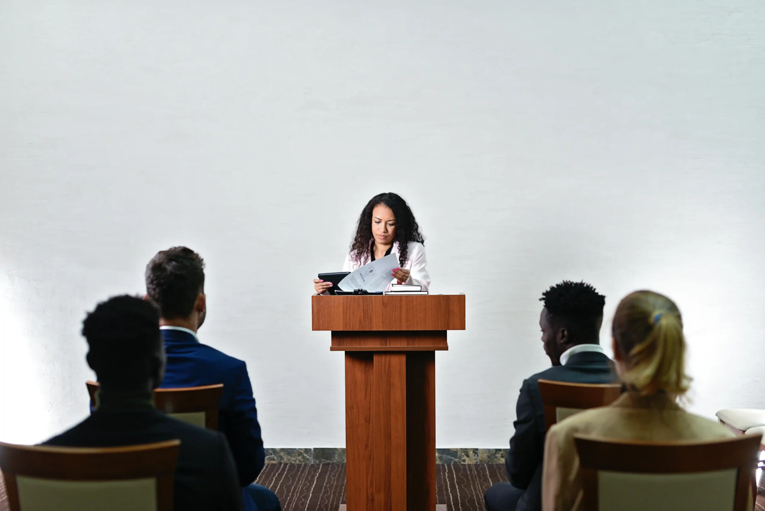 Woman standing at a podium presenting to an audience in a formal setting.