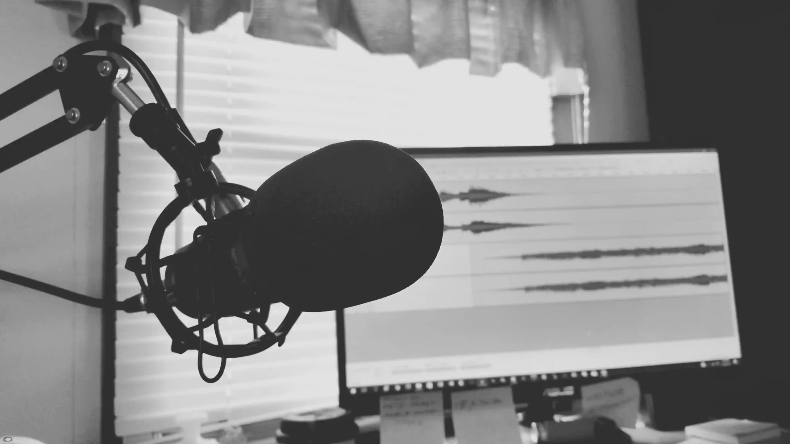 A close-up of a podcast microphone with waveforms displayed on a computer screen behind it.